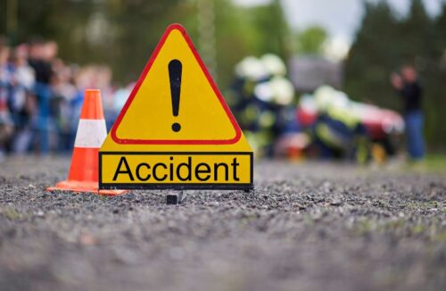 Close Up of Yellow Accident Sign and Orange Cone on a Road with Accident in the Background