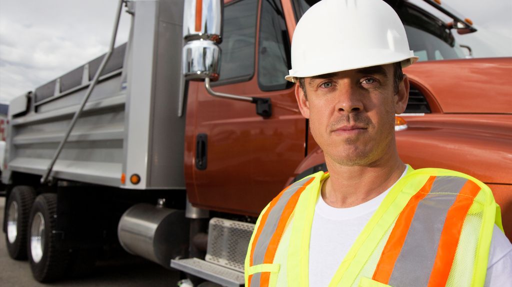 Truck Driver Next to a Semi Truck with Safety Vest and Hardhat